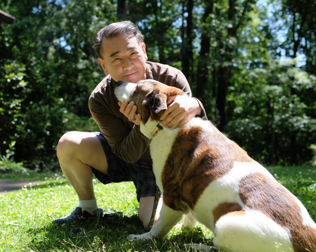 A man and a white and brown dog sitting in the yard on a very sunny afternoon