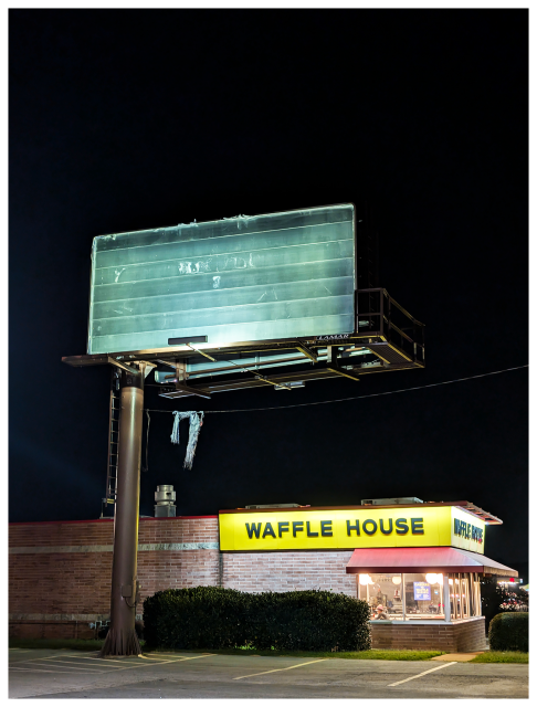 night scene. a weathered, empty billboard stands on a pole above a Waffle House restaurant, which glows with yellow and black signage, red canopy below