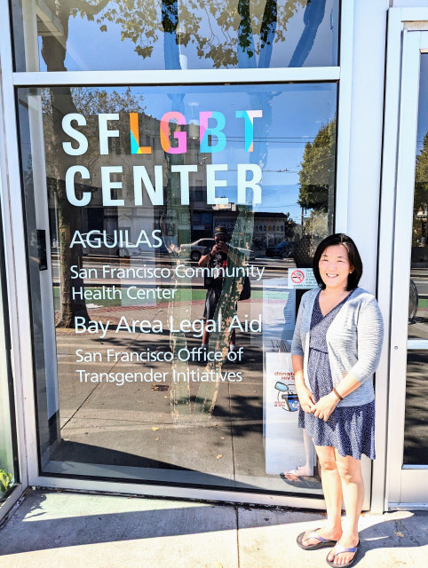 Joy standing in front of the SF LGBT Center in a dress and cardigan.
