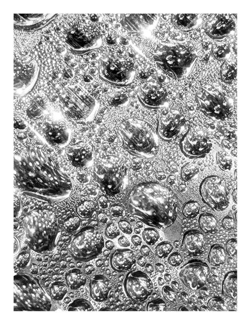abstract. raindrops on a black surface reflecting the sun.