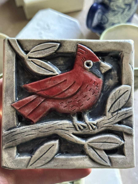 a ceramic tile with a red cardinal carved into the design. it's red and sitting on a branch