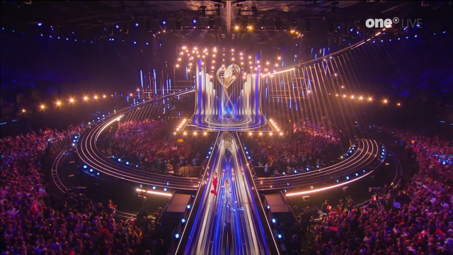 Lit up eurovision stage during the opening of the first semifinal. Lots of blinky lights and beams. Some audience around the stage