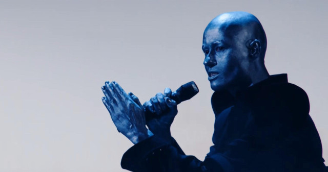Blue painted alien looking singer on white bg
