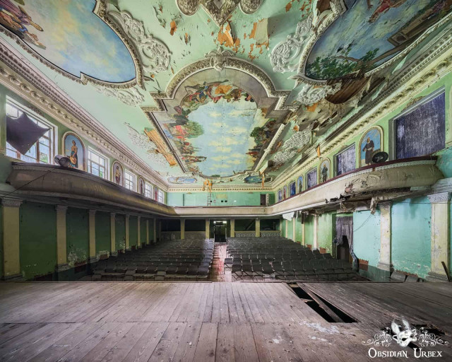 An abandoned Soviet-era culture house, featuring ornate but decaying murals and a dilapidated stage and seating.