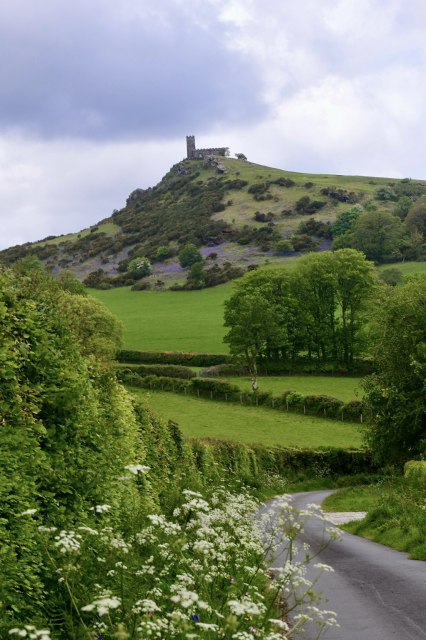A church on a hill with bluebells in the hills slopes. Cow parsley grows along the lane.