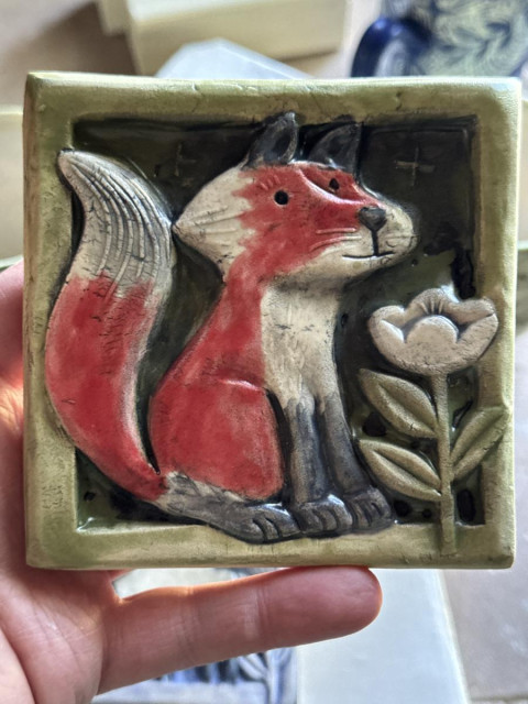 a handmade art tile depicting a fox looking at a flower