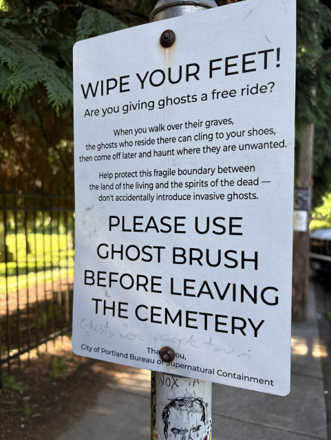 Photo of sign saying:

“WIPE YOUR FEET!
Are you giving ghosts a free ride?
When you walk over their graves,
the ghosts who reside there can cling to your shoes, then come off later and haunt where they are unwanted.
Help protect this fragile boundary between the land of the living and the spirits of the dead - don't accidentally introduce invasive ghosts.
PLEASE USE
GHOST BRUSH
BEFORE LEAVING THE CEMETERY
City of Portland Bureau of supernatural Containment”