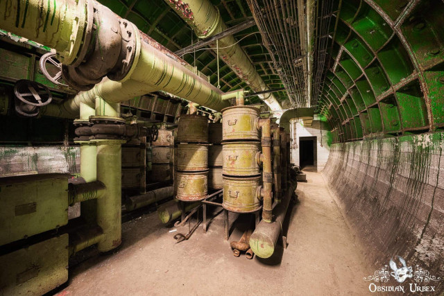 An abandoned, green-arched underground bunker features large pipes and rusty radioactive dust scrubbers.