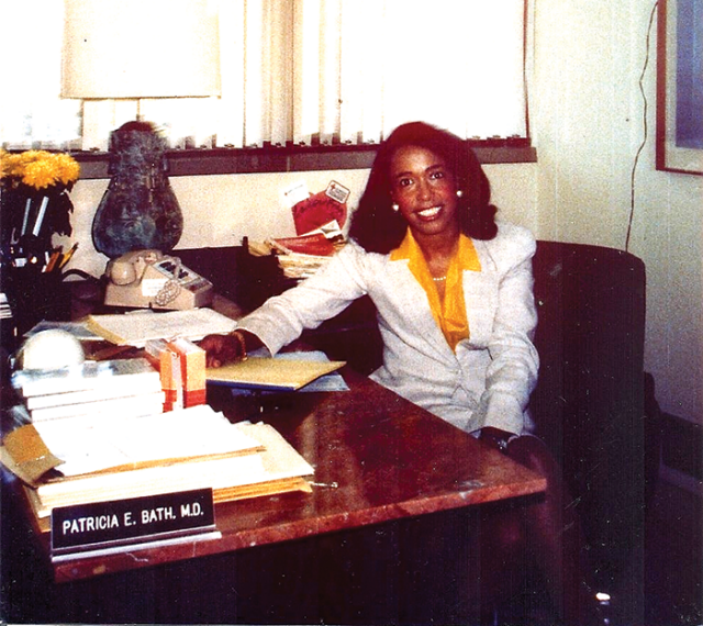 Snapshot of Patricia Bath at her desk in the 1980s. She's a Black woman with black hair in waves. 