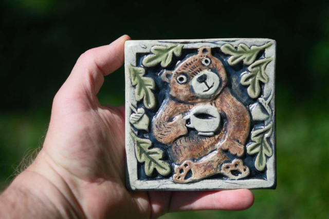 a photo of a handmade ceramic tile. the design is a bear holding a cup of tea (or coffee)