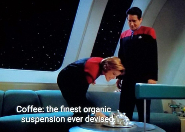 Star Trek Voyager scene. Commander Chakotay and Captain Janeway, both in uniforms, very profesh, are in her ready room standing next to a teal couch. Behind them is a large full wall window showing space and stars. I think I'd probably stand there a lot and just think about stuff. Janeway is bent over grabbing a cup from a tea kettle and set on the table. Closed caption reads, "Coffee: the finest organic suspension ever devised."
