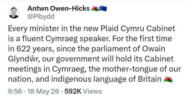 A screenshot of a  post on X (firmerly Twitter)  by Antwn Owen-Hicks with the handle @Pibydd, next to a Welsh flag and a European Union flag. The post includes a circular profile picture of a person. 

The text reads, "Every minister in the new Plaid Cymru Cabinet is a fluent Cymraeg speaker. For the first time in 622 years, since the parliament of Owain Glyndŵr, our government will hold its Cabinet meetings in Cymraeg, the mother-tongue of our nation, nation, and indigenous language of Britain 🏴󠁧󠁢󠁷󠁬󠁳󠁿". 

The bottom of the post displays "9:56 · 18 May 26 · 592K Views".