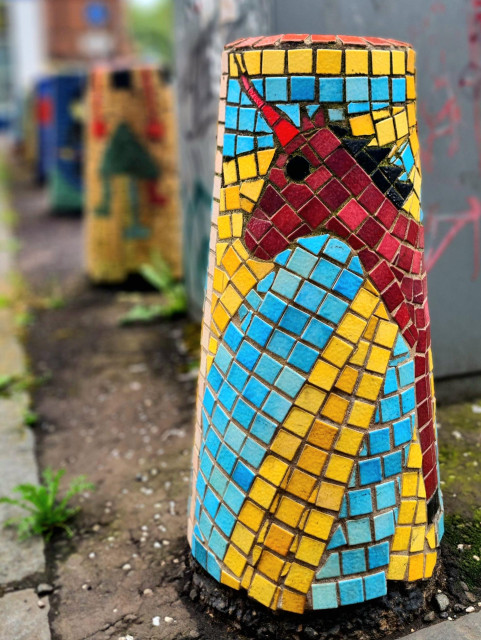 A mosaic of a unicorn against a sunburst covering a concrete bollard.