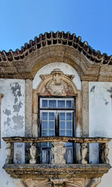 Old building window with stone masonry and a balcony.
Walls are white and the paint is peeling.
Place is Santa Comba Dão,  Portugal