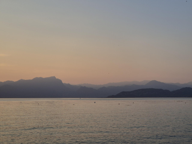 Sunset over a lake with layers of mountains in progressively more faded colours on on the horizon. 