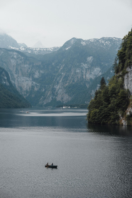 Mountain lake (Königsee) with steep forested slopes and two people in a small boat on the water