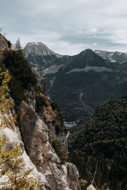 Mountain landscape with forested slopes, rocky outcrop in the foreground, and cloudy sky and the Königsee in the center