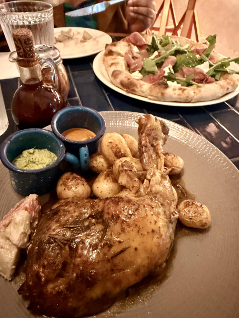 A photo of roast chicken and potatoes, and pizza in the background 