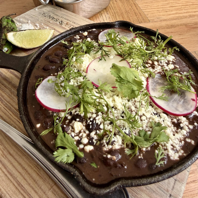 A photo of a small cast iron with black beans cheese, radish