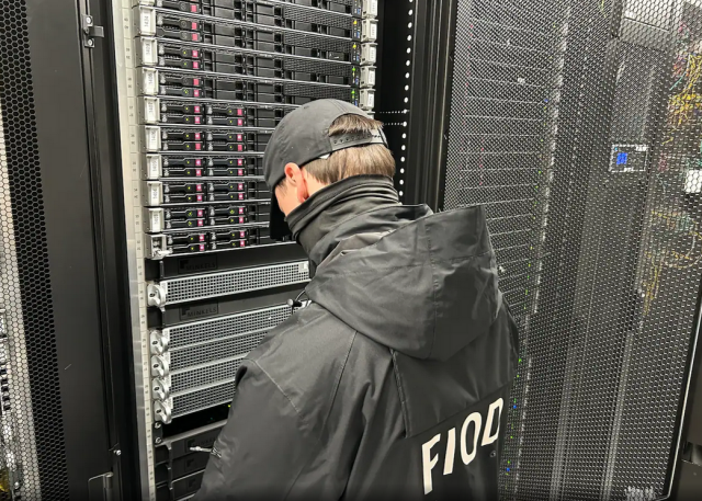 An investigator with the Tax Intelligence and Investigation Service (FIOD), the Dutch financial crimes agency, during the raid. Image: FIOD. We can see only the back of the person here removing drives from a server rack. The official is wearing a baseball cap and a black FIOD jacket.