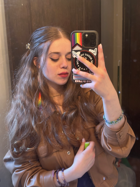 Mirror selfie of me wearing a pair of progress pride fringe earrings