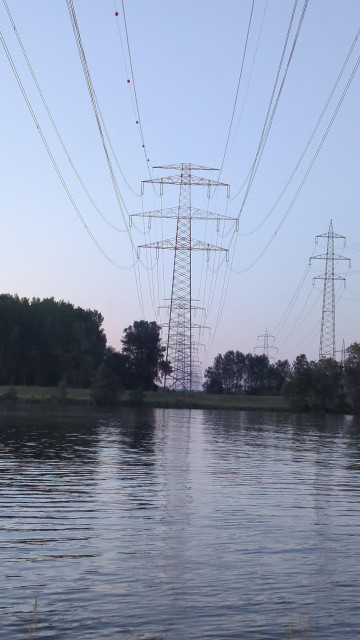 Hochspannungsnasten hinter einem Fluss in einer Reihe über einfn Fluss fotografiert