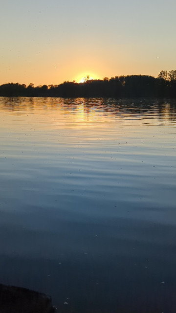 Die Sonne steht schon vom Horizont verdeckt über einrm Fluss mit faszinierendem Blau/gelb/orangem Farbenspiel