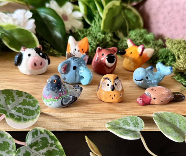 Picture of 9 handmade clay figurines representing different animals (pigeon, cat, elephant, owl, cow, shark, platypus, fox, and bear).