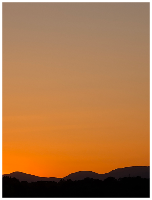 a vivid sunset sky with a gradient from deep orange at the horizon to light gold and soft gray above, silhouetting dark rolling hills and scattered treetops in the foreground.