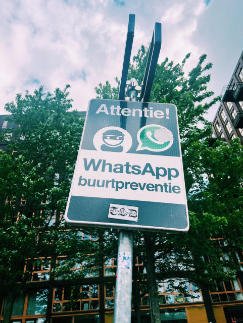 A photo of a street sign with the drawings or a thief and the WhatsApp logo and a message in Dutch that seems to warn about something 