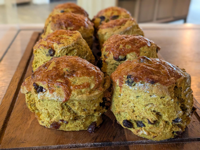Colour photograph of eight golden brown scones topped with melted cheese on a wooden platter. 