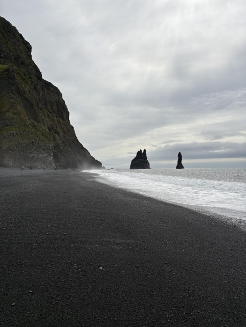 A cliff and black sand beach approach a vanishing point: sea stacks step out into the Atlantic. 