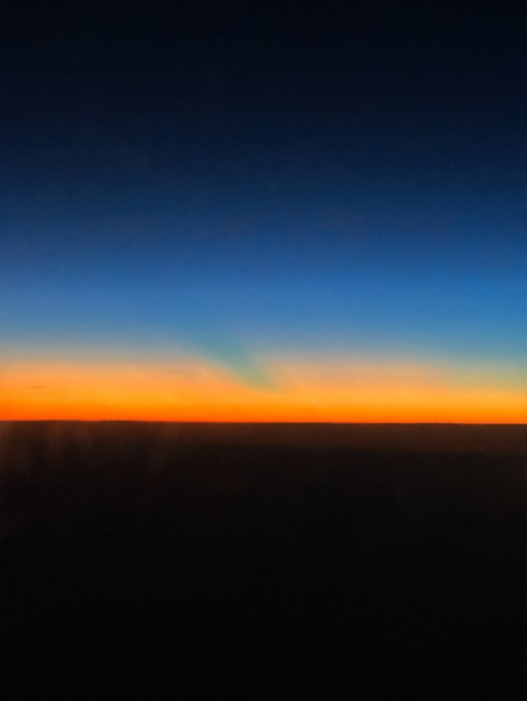the gradient of the sunset in the sky: from orange at the horizon, to a brighter yellow-orange shaped as if layers of cloud, soon giving way to a turquoise that fades to deep blue and ultimately black. Below that, the ground is a dark plane
