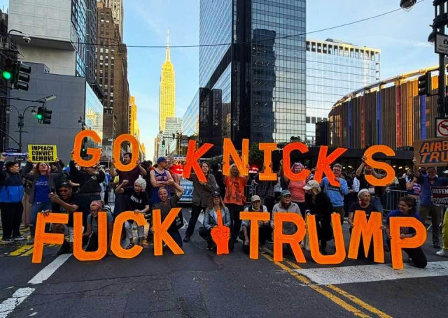 A crowd of protesters greet the motorcade with large orange letters that read Go Knicks Fuck Trump 