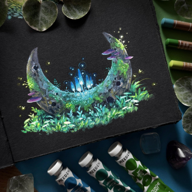 A photo of an open black paper sketchbook, with only half the page visible, placed on coloured paper and surrounded by gouache tubes, coloured pencils, leaves, and crystals. The sketchbook page shows a painting of a petrified sickle moon, fallen onto a patch of lush greenery. Moss and different kinds of mushrooms grow on the moon. In the crook of the moon glowing blue mushrooms grow, making up the main focus.