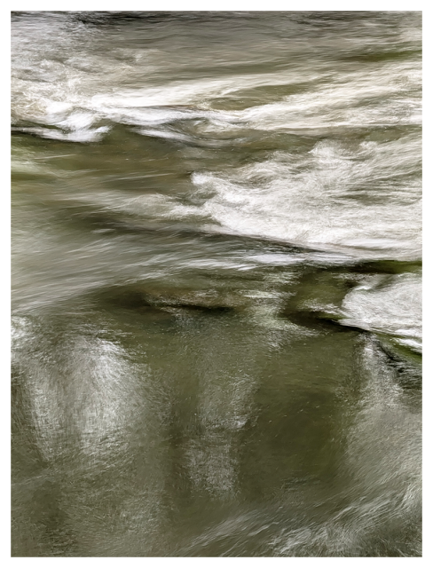 abstract. soft-focus photo of a flowing river, with gentle ripples and white foam on the surface. the water appears greenish-brown, reflecting tree shapes above. 