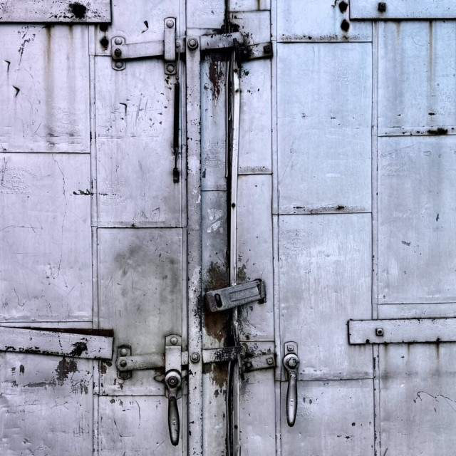 Metal door on a patio with a series of handles and locking devices and a bit of rust