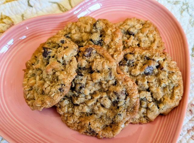 Five chocolate chip and oatmeal cookies on a pink heart shaped plate. 