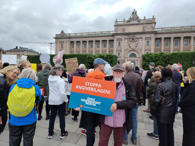 Person med skylt Stoppa Angiverilagen. Flera demonstranter framför riksdagshuset