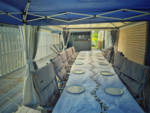 Our new outdoor seating area, with a long table, 12 chairs, under a pavilion which stands on our decking.