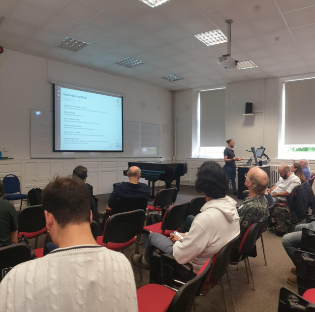 A photo taken from the perspective of the audience showing the author, Giulio Gabrieli, standing at the front of the room. The presenter is gesturing while speaking about a projected slide titled 'Machine Learning Model' at the LAC2026 conference in Maynooth.