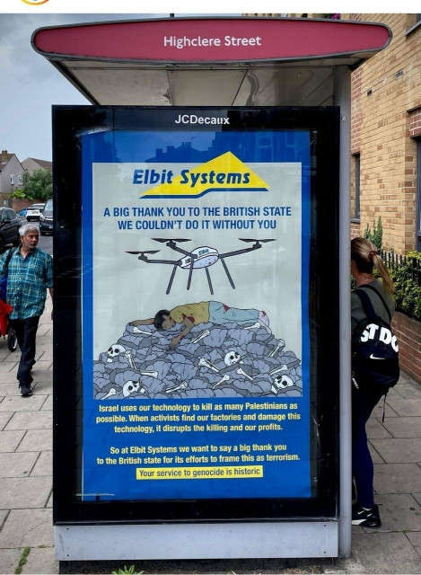 Subvertising Elbit poster on a bus stop shows cartoon of death-dealing drone above mound of bodies and text expressing their gratitude to the British state. Tagline reads 'your service to genocide is historic' 