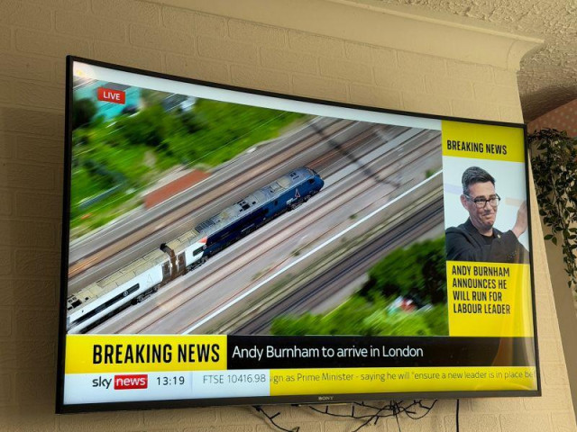 Photo: wall mounted TV with Sky's airborne coverage of a train (we must assume Andy Burnham is on it) with the headline 'Breaking News: Andy Burnham to arrive in London'