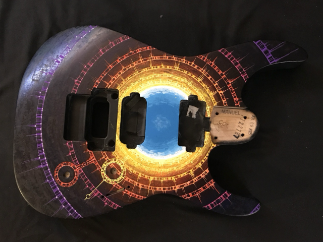 Front view of strat body WIP painting showing concentric rings in purple thru bright yellow to white surrounding a blue circle, part representation of a supernova blast