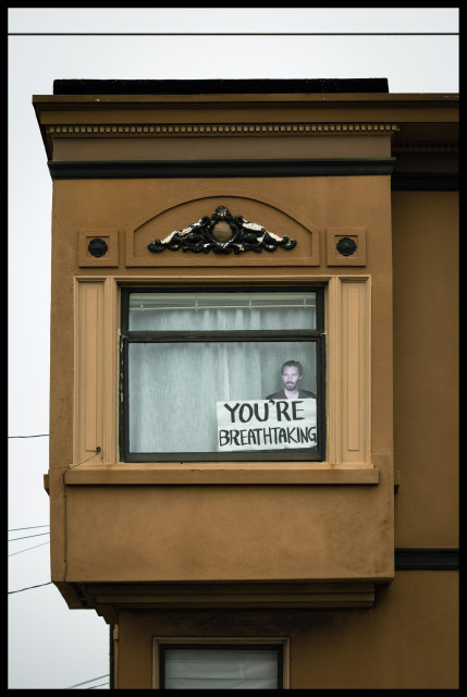 A picture of a large window in a tan colored stucco Victorian apartment building in San Francisco. While the room inside the apartment is hidden by a white curtain, there is still something to be seen. Between the curtain and the glass is a large, poster-sized cut-out of Keanu Reeves holding up aside that says YOU'RE BREATHTAKING.

Keanu is right, as always.