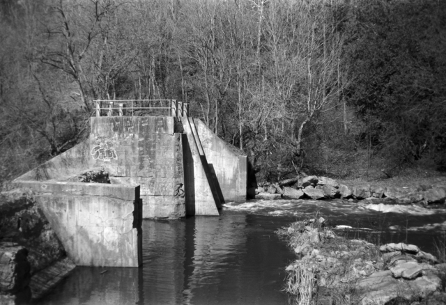 Concrete remnants of a mill mostly block a small river. 