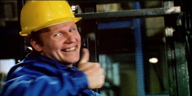 Klaus, from the classic German safety video "Staplerfahrer Klaus" (Forklift Driver Klaus). He is a white man wearing a blue shirt, has a big smile on his face, and is flashing a thumbs up. If his coworkers aren't all dead, they soon will be.

Like Engineercat above, Klaus is sitting in a warehouse and wearing a hardhat.