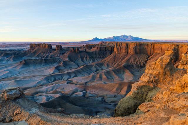 The sun casts an orange glow on cliffs overlooking a barren, rocky landscape.