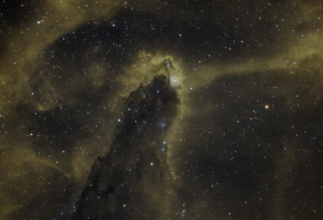 A towering pillar of dark dust is silhouetted by glowing gas all around it.