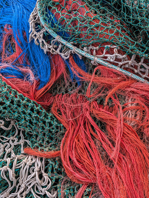 A tangled, chaotic jumble of commercial fishing nets. The composition is packed with contrasting textures and vivid colors, creating a complex visual pattern.
